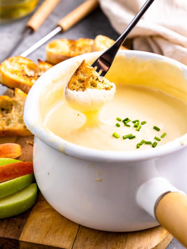 three-quarters view of a piece of grilled bread being dipped into a pot of fondue with a long fork.