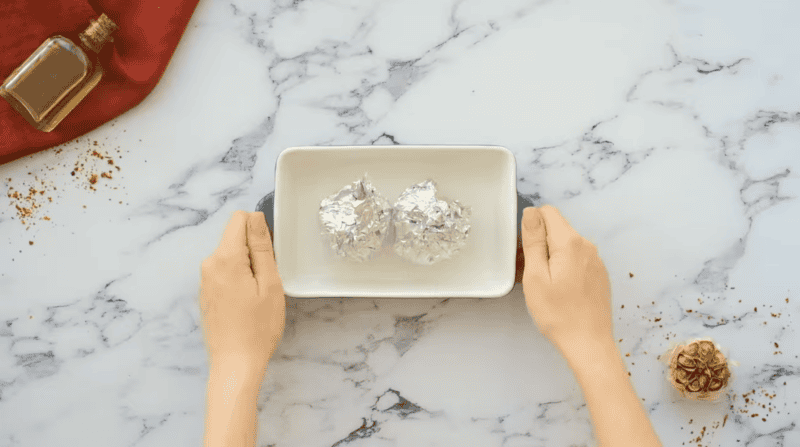 2 heads of garlic wrapped in aluminum foil in a small baking dish.