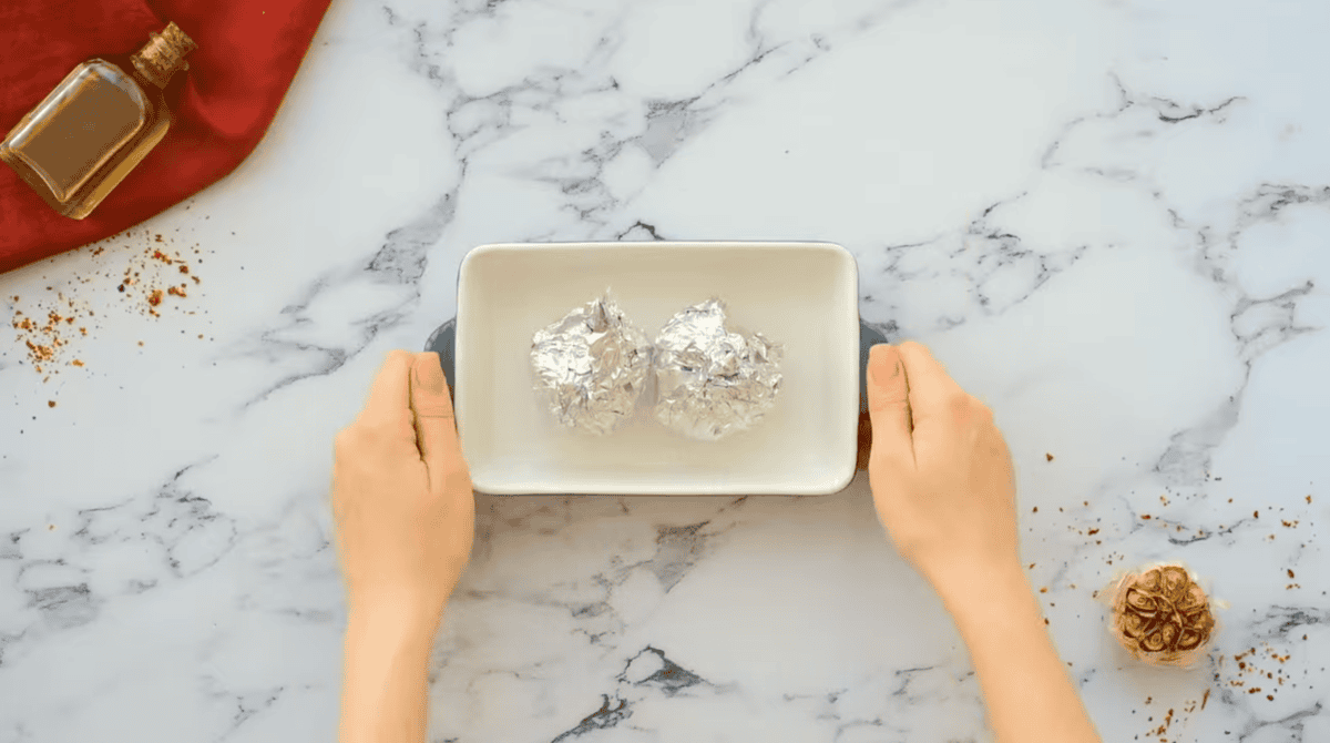 2 heads of garlic wrapped in aluminum foil in a small baking dish.