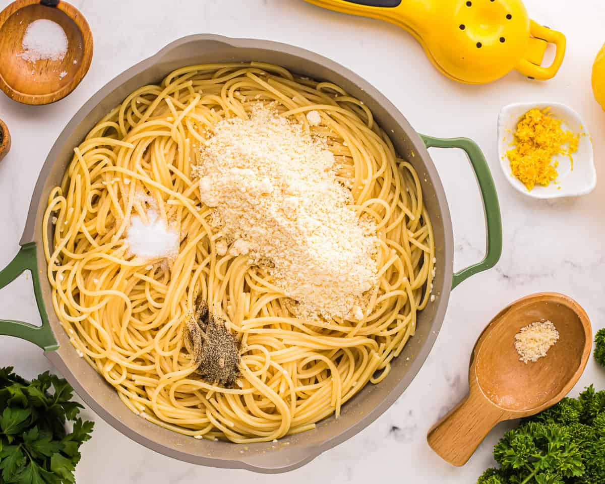 a pan of spaghetti with parmesan cheese, parsley, and other ingredients.