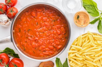 a pan with tomato sauce and pasta on a white background.