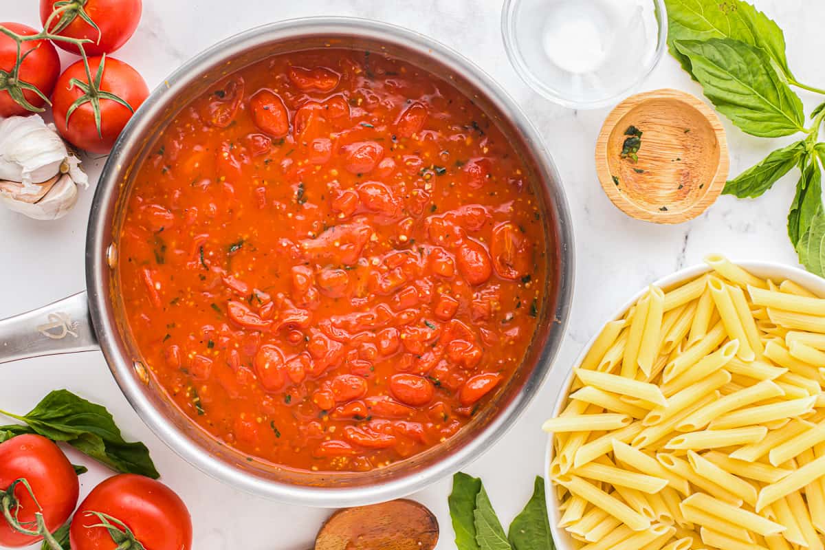 a pan with tomato sauce and pasta on a white background.