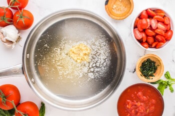 a frying pan with tomatoes, garlic, basil and other ingredients.