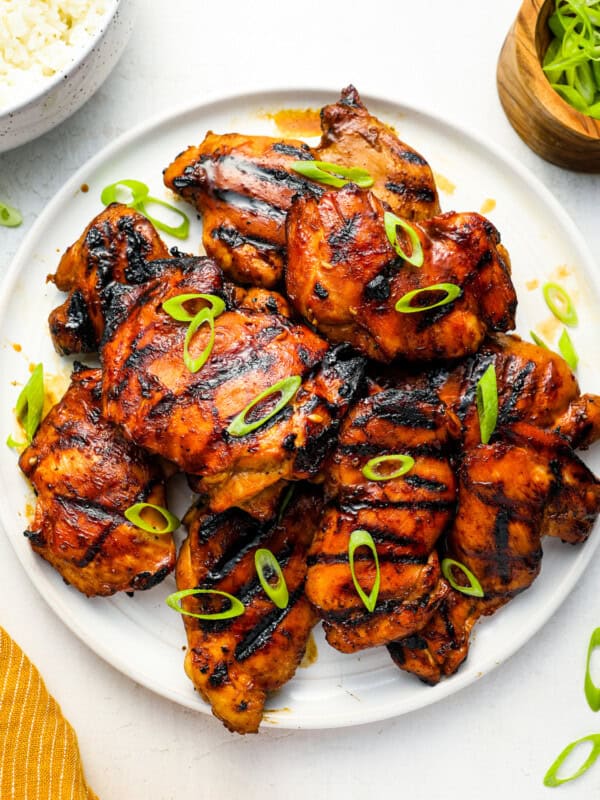 overhead view of grilled huli huli chicken thighs on a white plate topped with green onions.