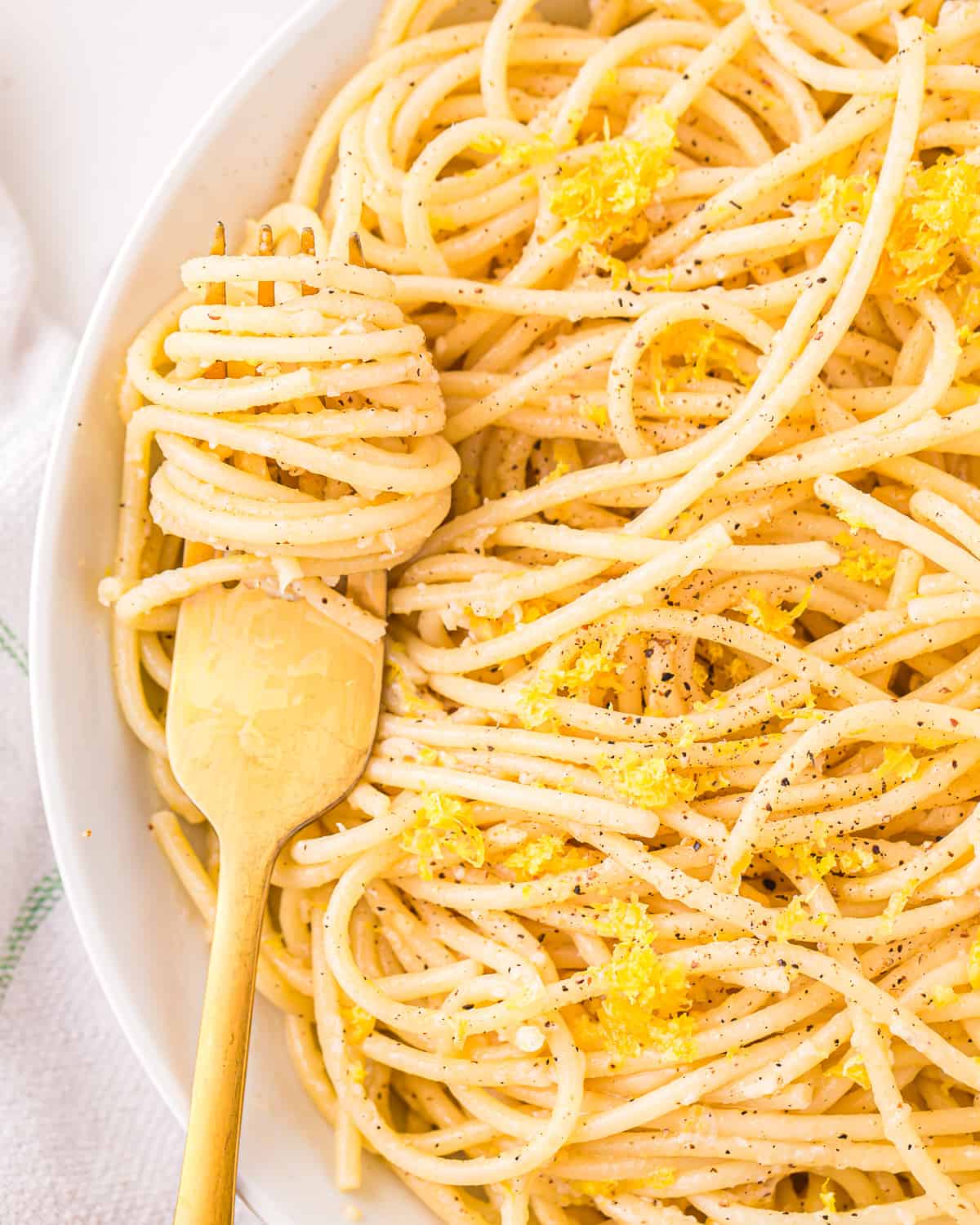 close up on a bowl of lemon butter pasta, garnished with black pepper and lemon zest.