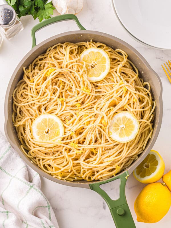 a green skillet filled with pasta and lemons.