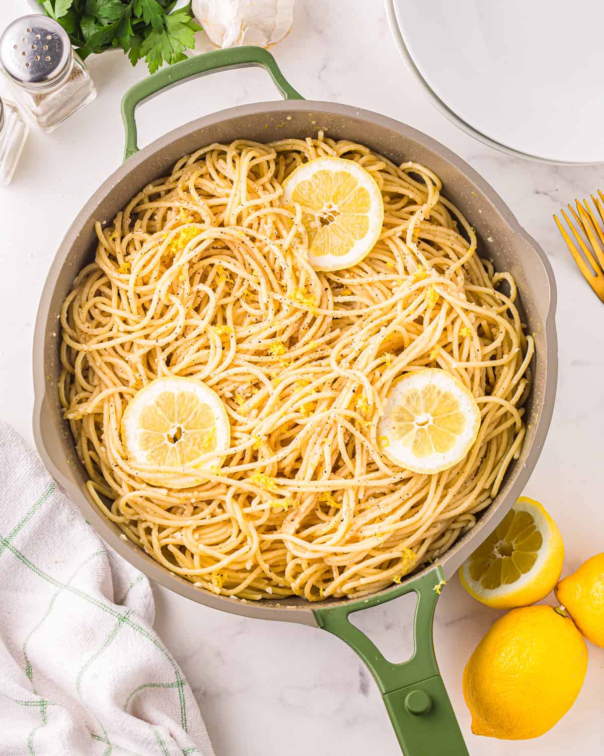 a skillet filled with lemon pasta, garnished with slices of lemon and lemon zest.