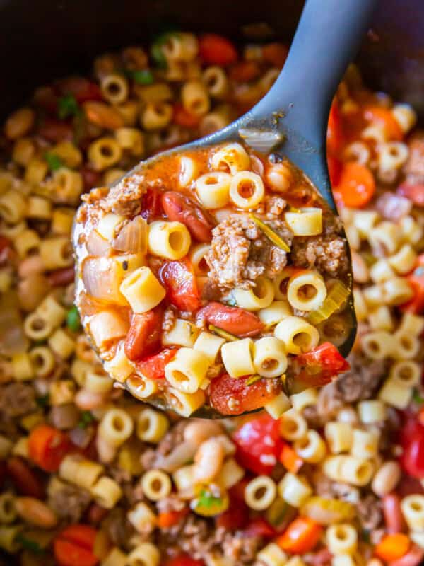 close up view of a spoonful of pasta e fagioli soup above a pot.