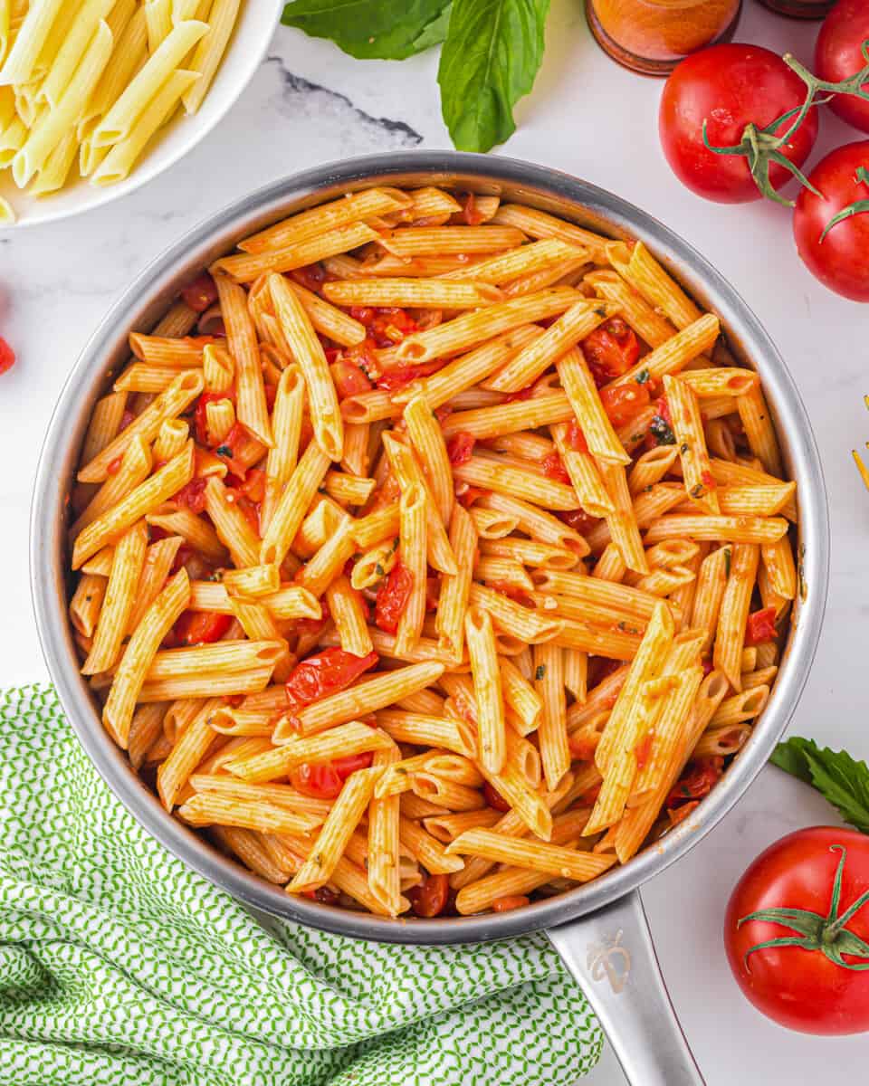 penne pasta in a pan with tomatoes and basil.