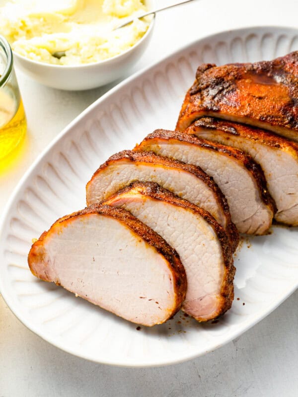 three-quarters view of a sliced smoked pork loin on a white oval serving platter.