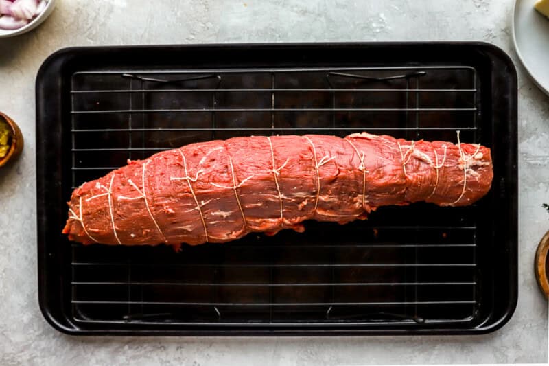 tied beef tenderloin on a wire rack set in a baking sheet.