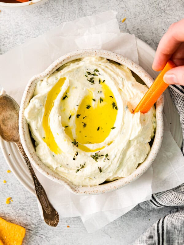 overhead view of a hand dipping a carrot stick into whipped feta dip with olive oil on top.