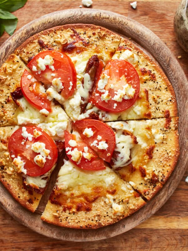 overhead view of a cut white pizza on a round wooden cutting board.