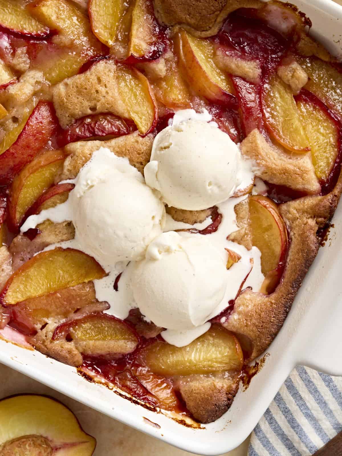 overhead view of scoops of ice cream on peach cobbler in a baking dish.