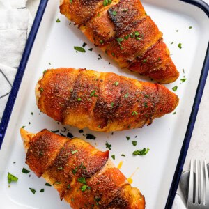 three chicken breasts on a baking tray with a fork.