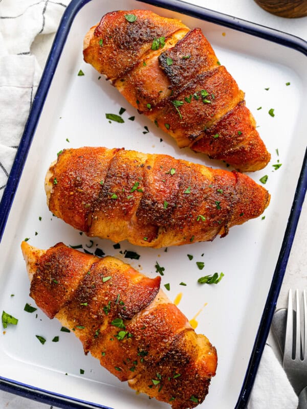 three chicken breasts on a baking tray with a fork.