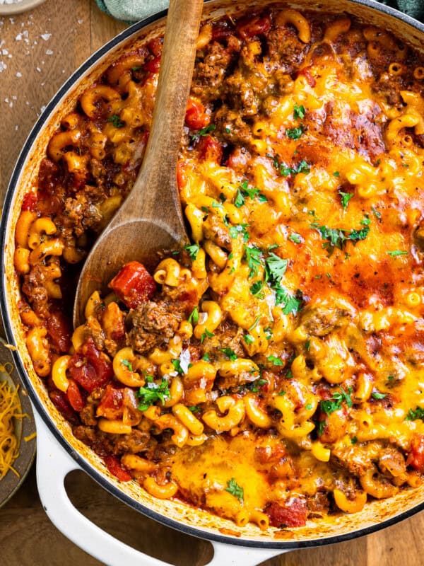 cheesy goulash in a pan with a wooden spoon.