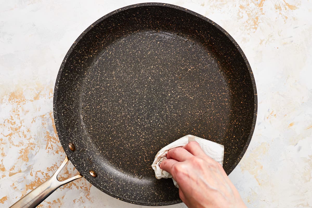 A hand wiping out a skillet with a paper towel.