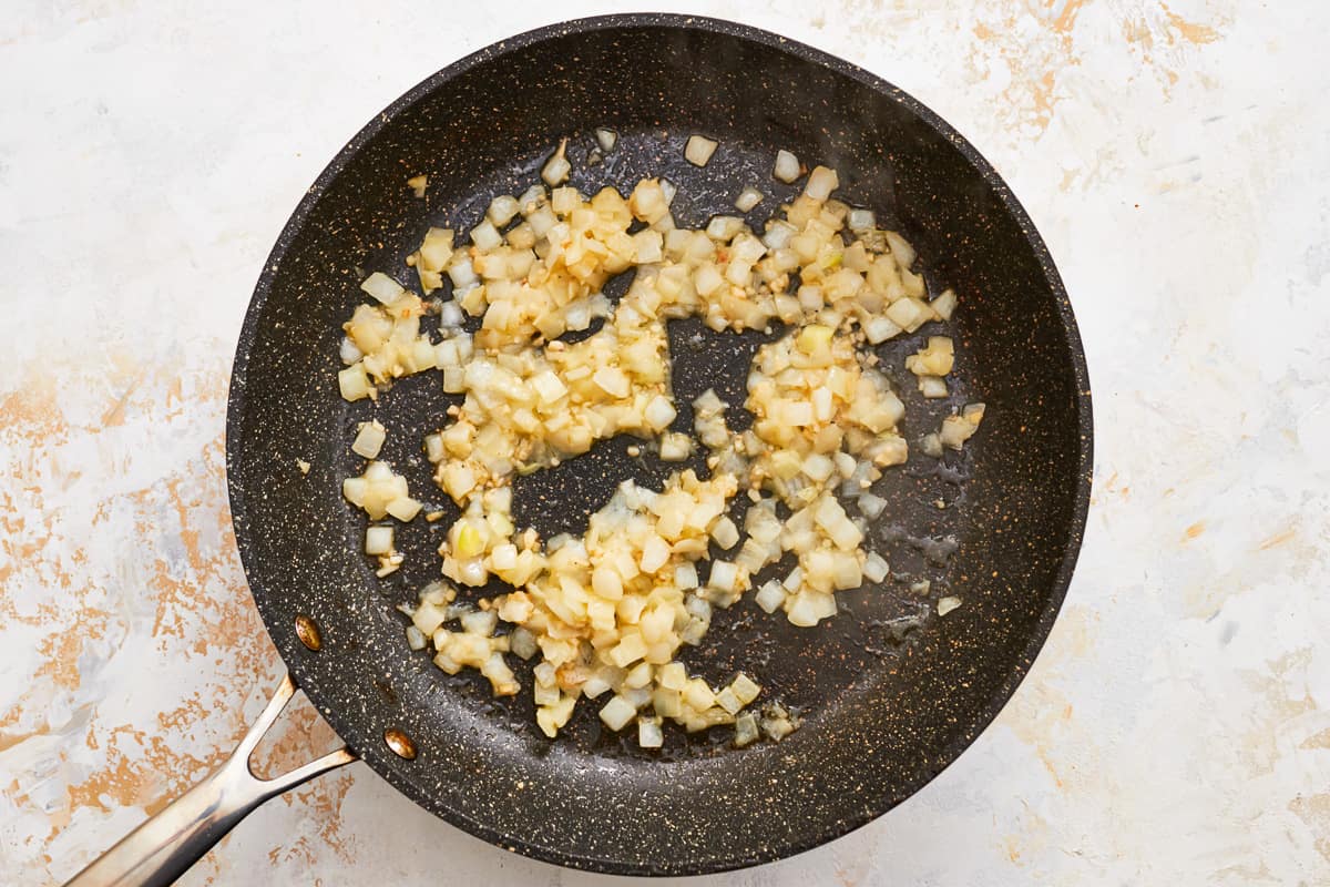 Diced onion and minced garlic cooking in a skillet.