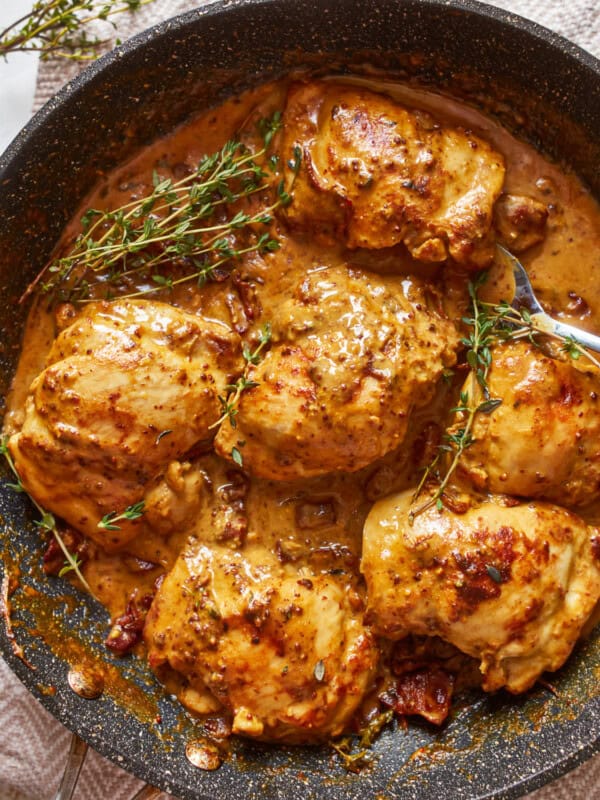 chicken breasts in a pan with sauce and sprigs of thyme.