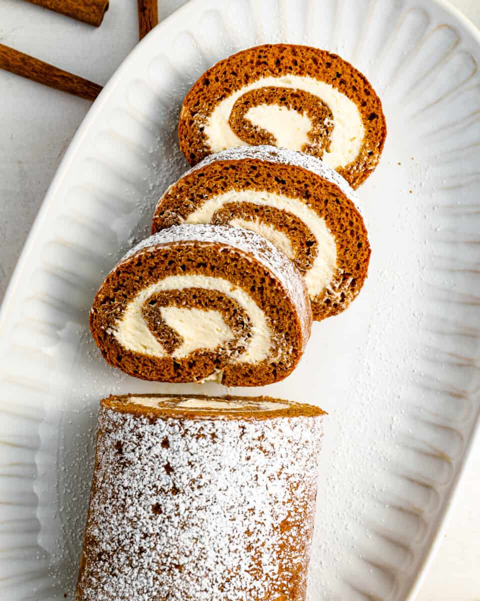 a pumpkin cake roll with powdered sugar on a white plate.