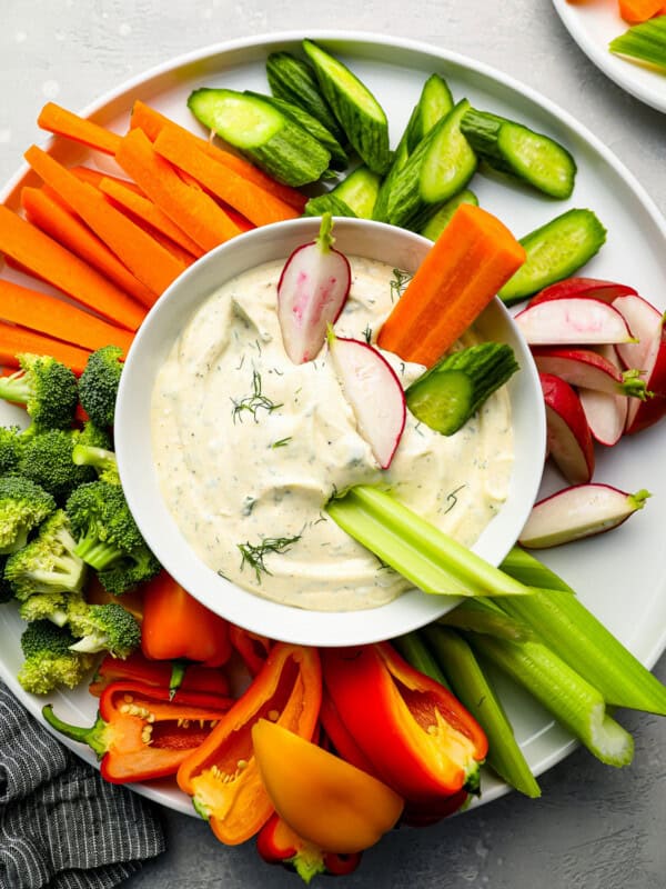 a plate of dip with vegetables and radishes.