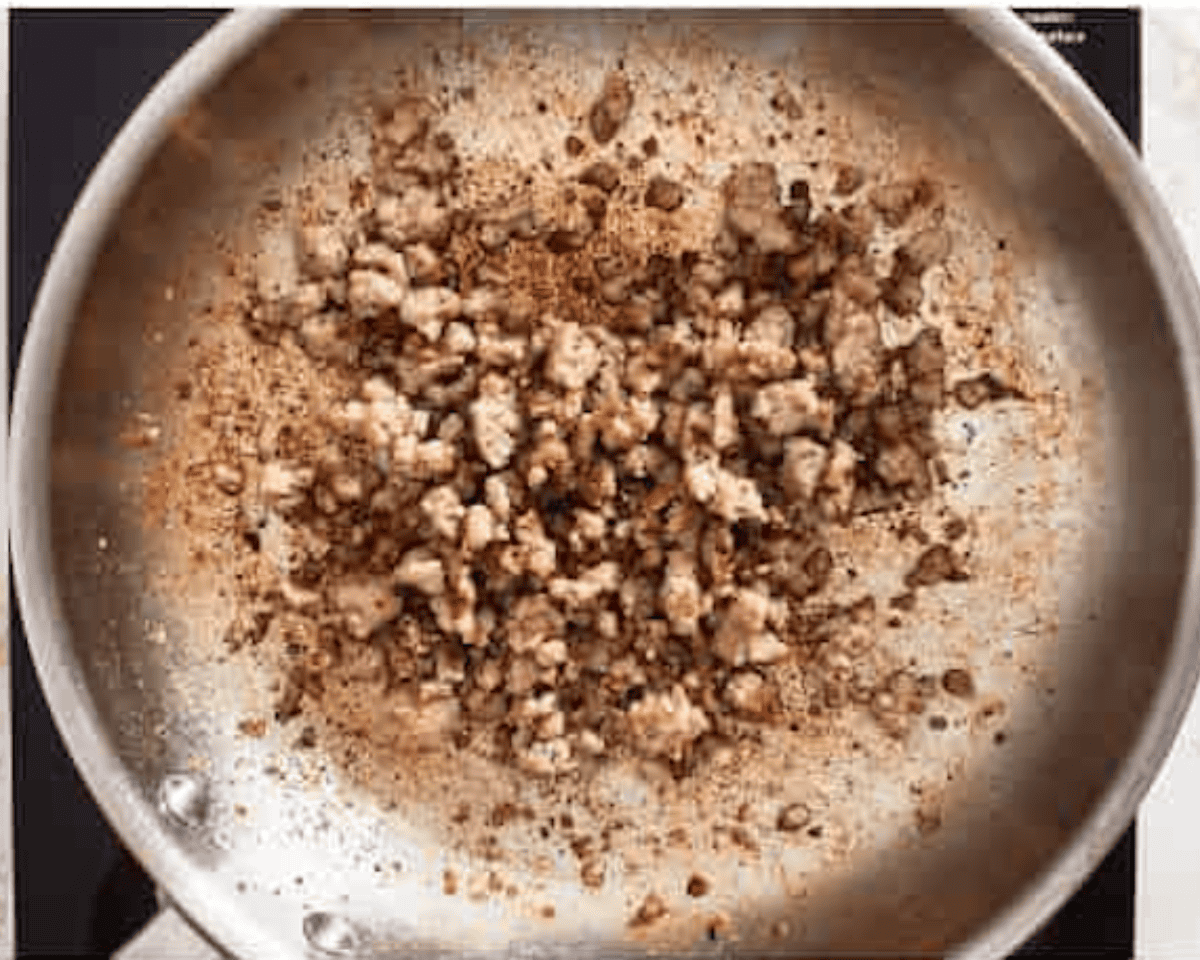 A stainless steel skillet with browned sausage crumbles and seasonings on the surface.