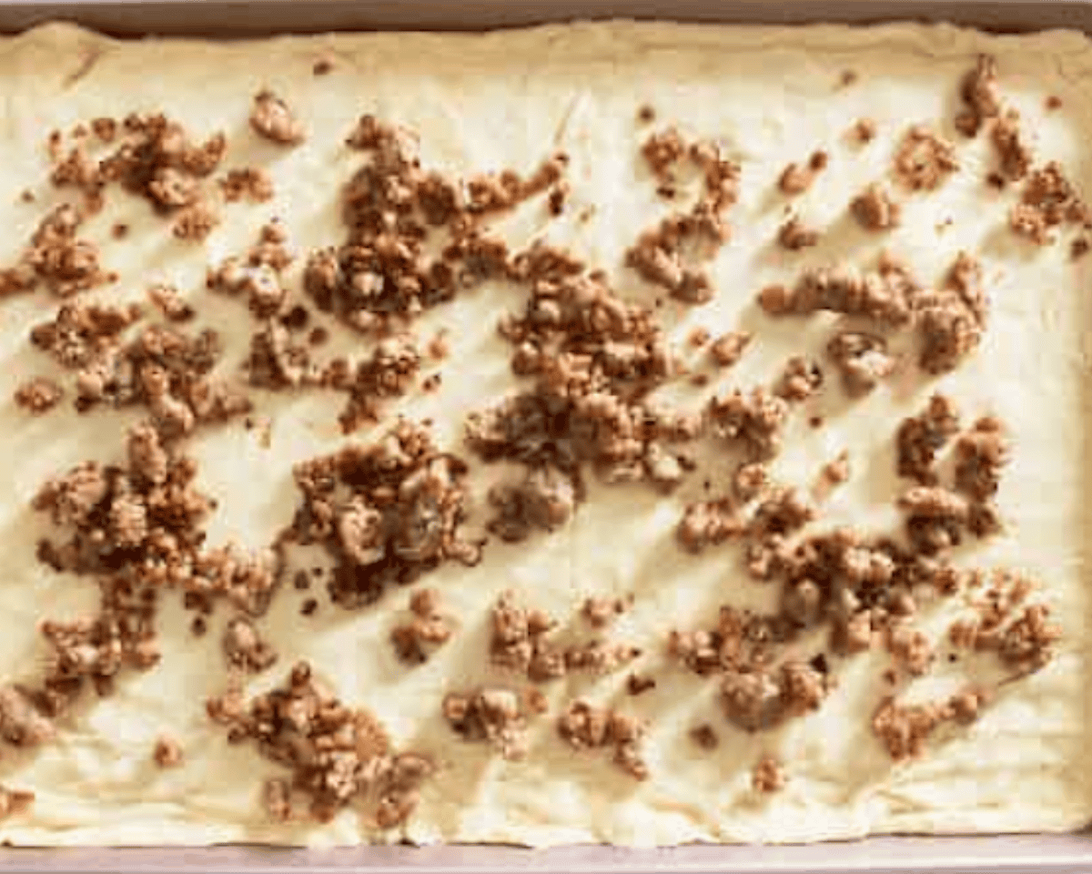 A baking pan lined with crescent roll dough, topped with scattered cooked sausage crumbles.