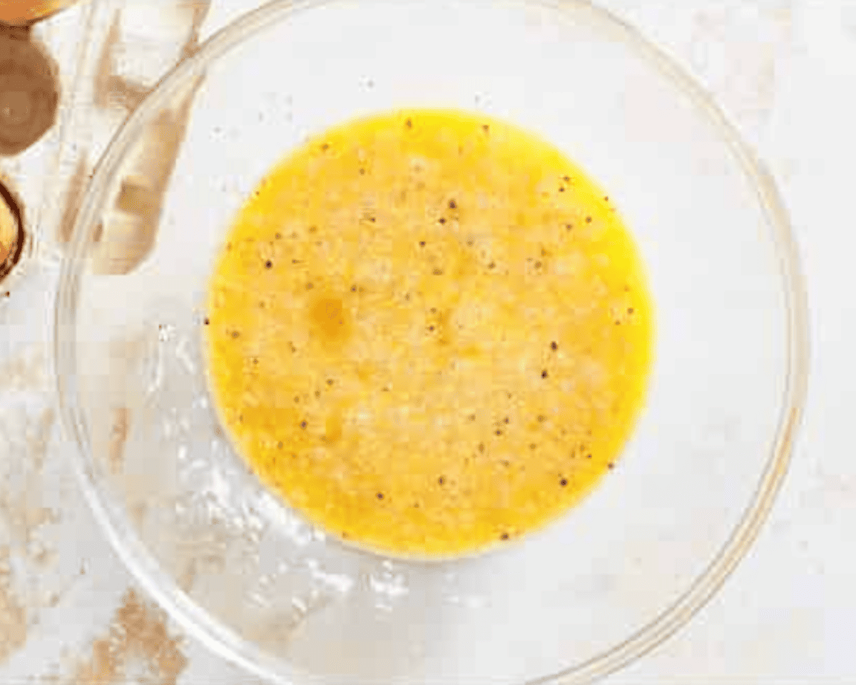 A glass bowl filled with a whisked egg mixture, speckled with black pepper and Parmesan cheese.