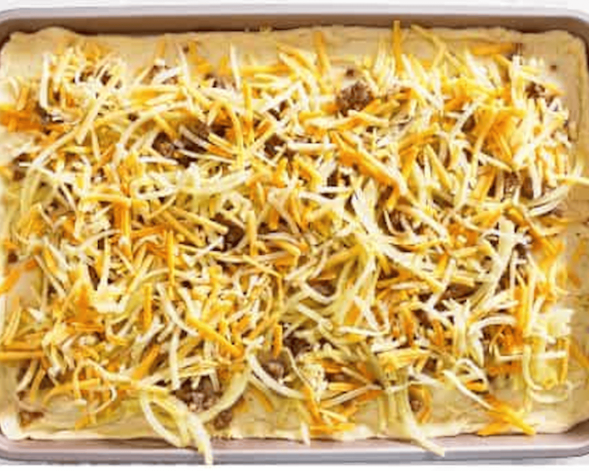 The baking pan with the sausage and hash brown layers, now topped with shredded cheese.