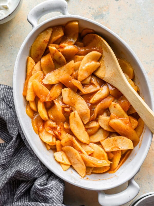 Apples in a dish with a wooden spoon.