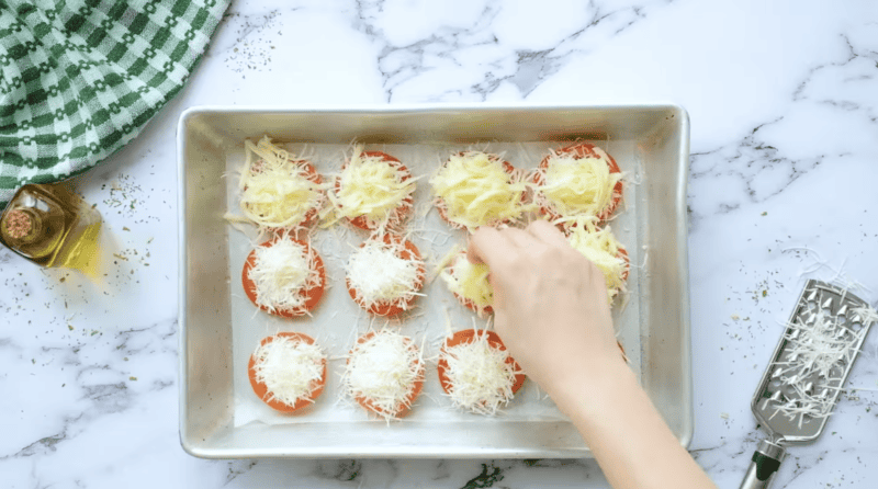 sprinkling mozzarella cheese over parmesan-topped tomato slices.