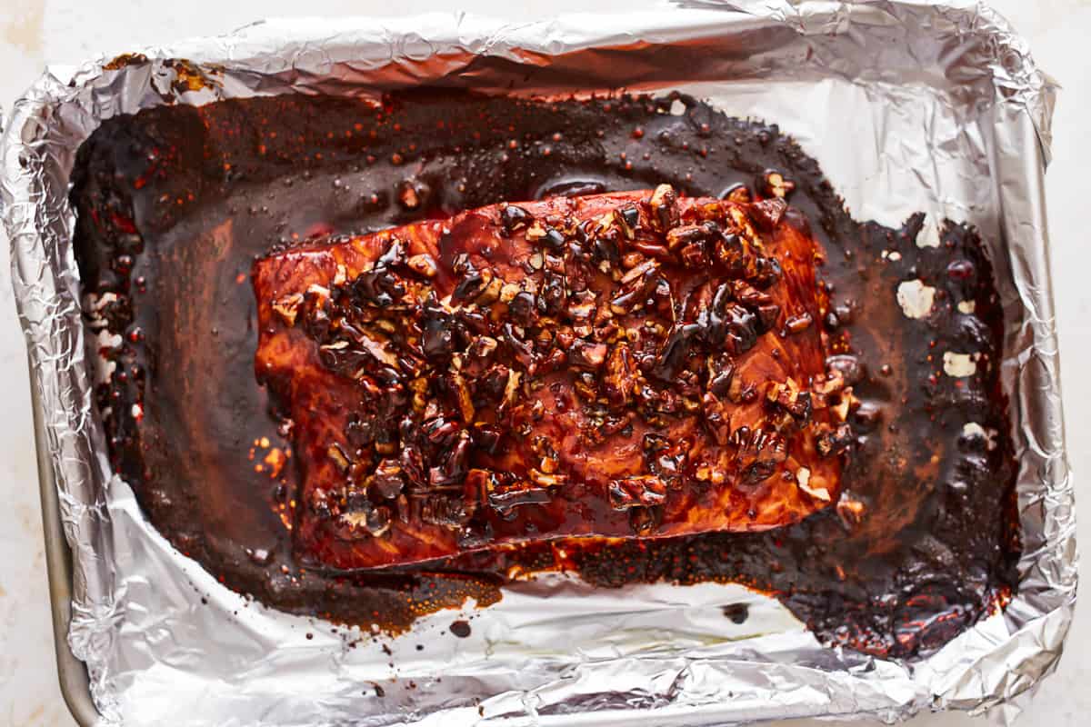 A piece of salmon on a sheet of foil topped with bourbon brown sugar glaze and pecans.