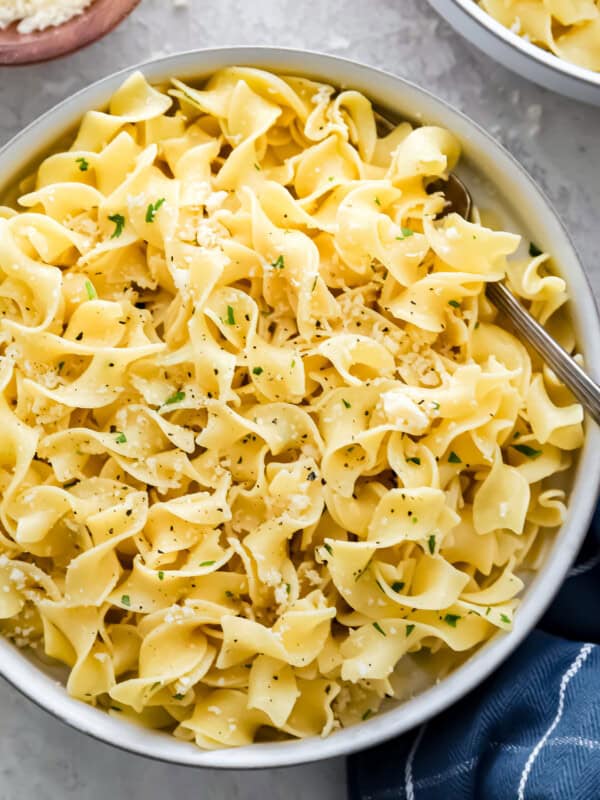 Two bowls of pasta with parmesan cheese and parsley.