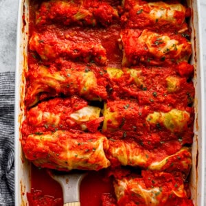 Stuffed cabbage rolls in a baking dish with a wooden spoon.