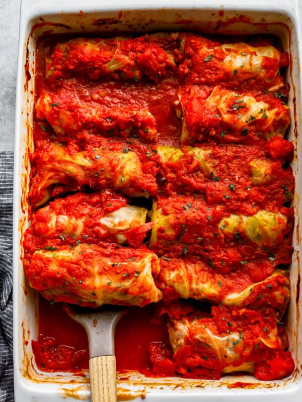 Stuffed cabbage rolls in a baking dish with a wooden spoon.