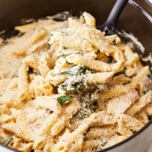 A pot of pasta with cheese and spinach in it.