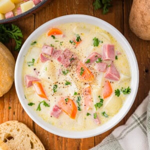 A bowl of soup with potatoes, carrots and ham.