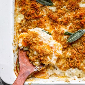 A casserole dish with a spoon and a sprig of sage.