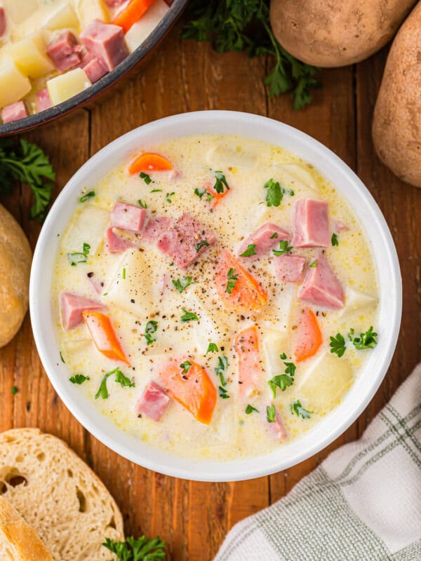 A bowl of soup with potatoes, carrots and ham.