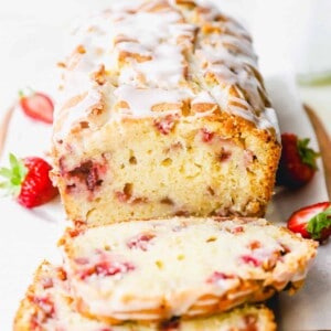 three-quarters view of sliced strawberry bread on parchment paper on a wooden cutting board with two slices laying in front of it.