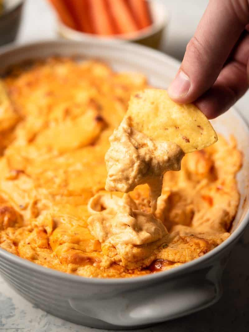 A person dipping a chip into a bowl of buffalo chicken dip.