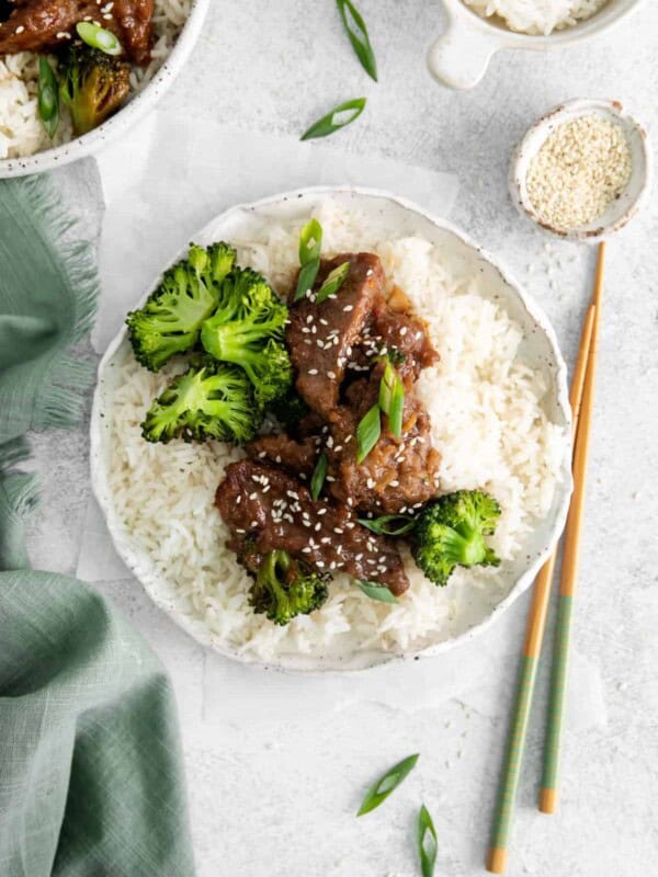 overhead view of instant pot mongolian beef over rice on a white plate with chopsticks.