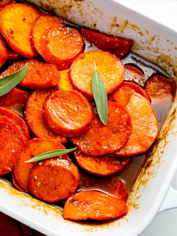 A white baking dish filled with sweet potatoes and sage.