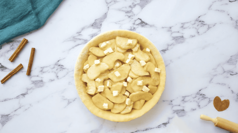 a pie crust filled with sliced apples dotted with cubes of butter.