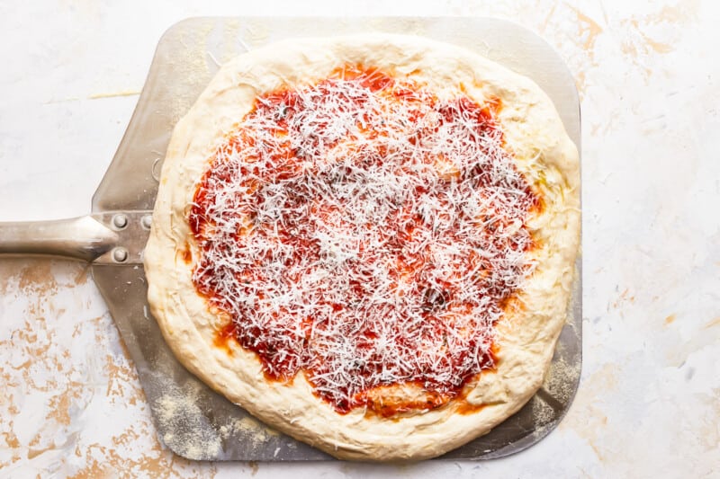 A pizza with sauce and cheese on a baking sheet.