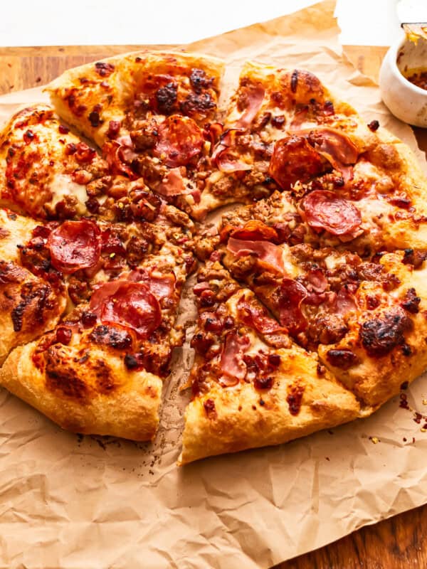 A cut meat lovers pizza on parchment paper.