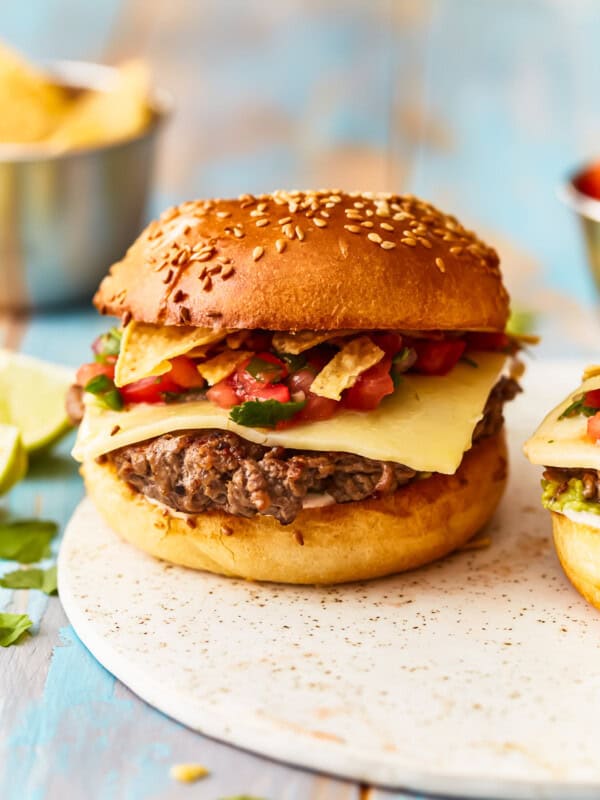 Two burgers on a plate with chips and salsa.