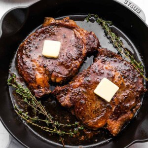 overhead view of oven baked steaks in a cast iron pan topped with a pat of butter and thyme.