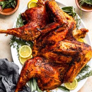 A roasted turkey on a plate with lemons and sprigs of thyme.